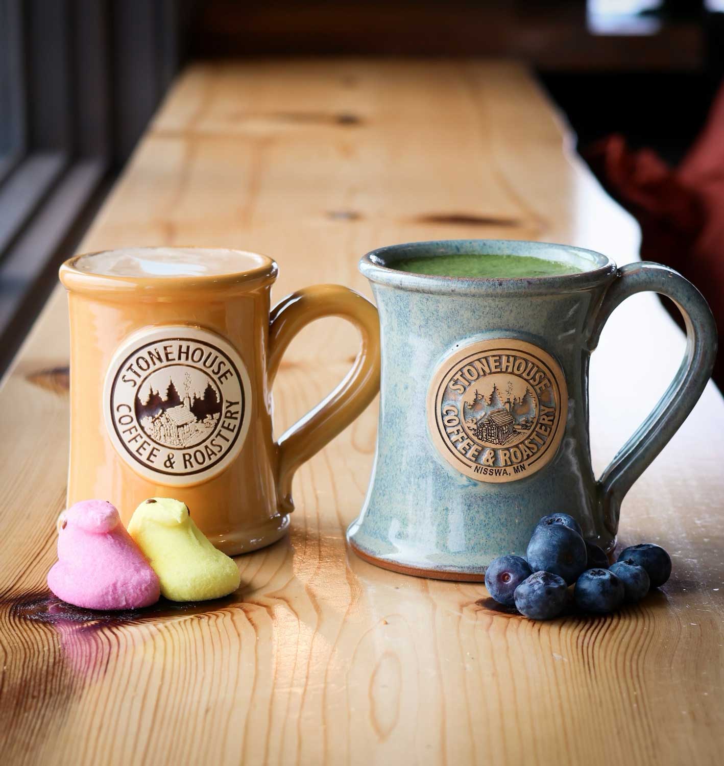 Two Stonehouse Coffee & Roastery mugs on a wooden table with marshmallows and blueberries.