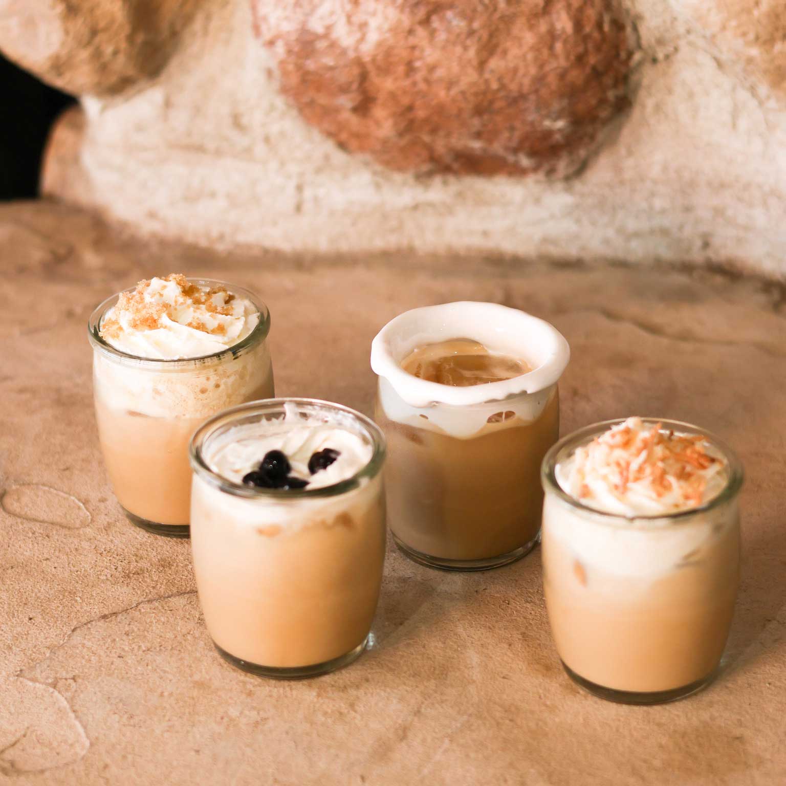 Four small glass jars with various desserts on a stone surface