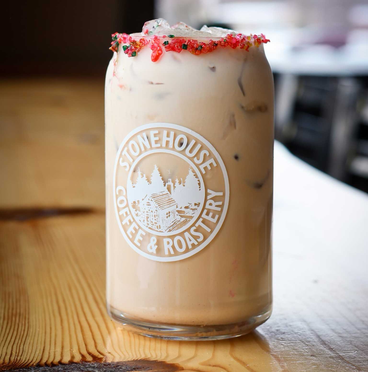 Iced coffee in a glass with a 'Stonehouse Coffee & Roastery' logo on a wooden surface.